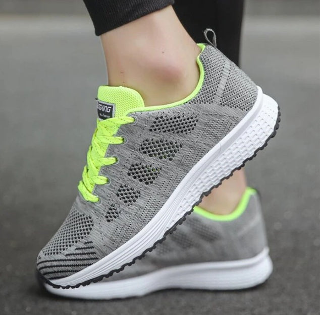 Women wearing lightweight grey and neon yellow breathable athletic sneakers on a street surface