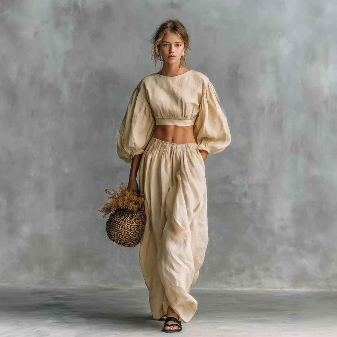 A woman wearing a beige two-piece set featuring a cropped puff-sleeve top and wide-leg trousers with pockets.