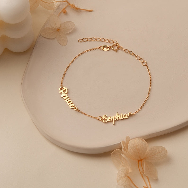 Close-up of a personalized gold-toned name bracelet with a minimalist design on a neutral background.