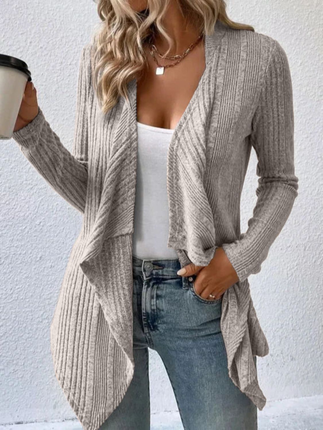 A woman wearing a heather grey, long sleeve, open front, ribbed cardigan over a white top and blue jeans.