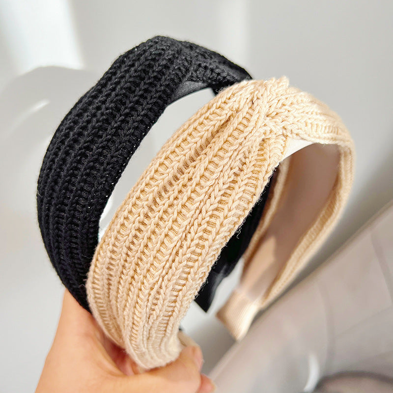 A collection of wool knit wide headbands in black, beige, cream, and brown, featuring a subtle twisted design, displayed on a clean surface.