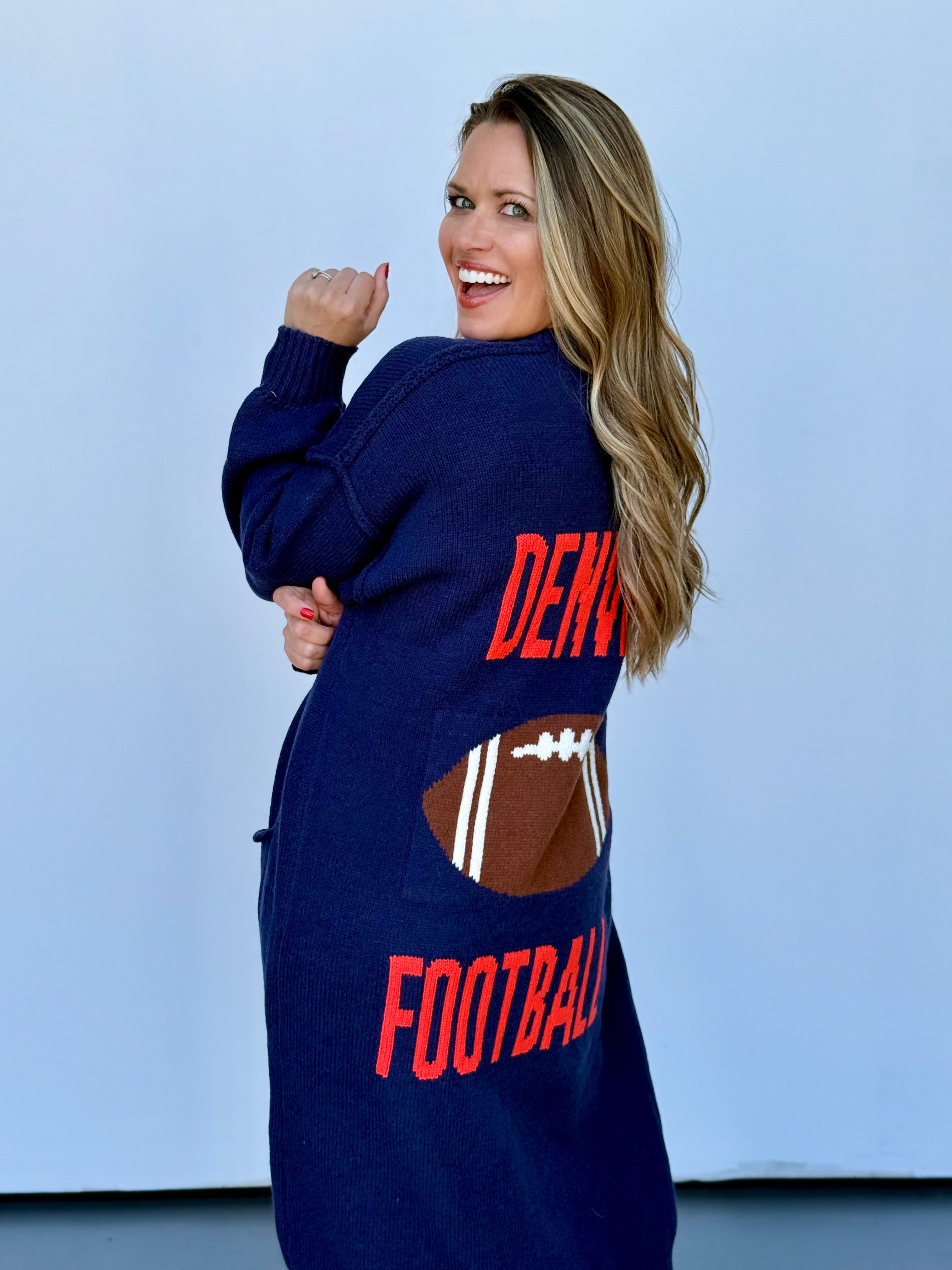 Woman wearing a cozy navy blue, orange, brown, and white knit cardigan for football game day.