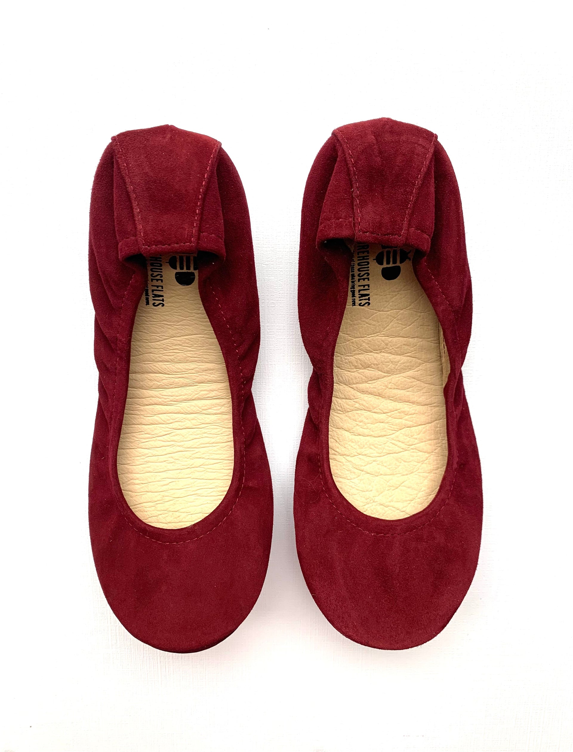 Top-down view of a pair of wine-colored suede ballet flats, followed by a view of the rubberized grip soles featuring The Storehouse Flats logo.