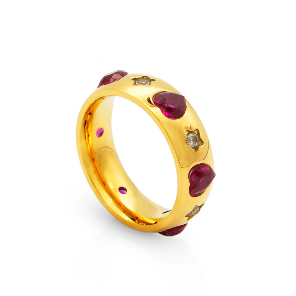 A close-up of a brilliant gold XOXO Love Ring featuring inlaid heart-shaped ruby gemstones and star-shaped diamonds, shown on a clean white background.