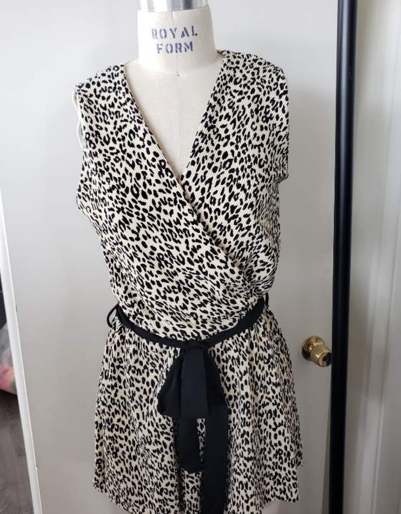 Model wearing a sleeveless cream and black leopard print mini romper with a tie waist and V-neckline.