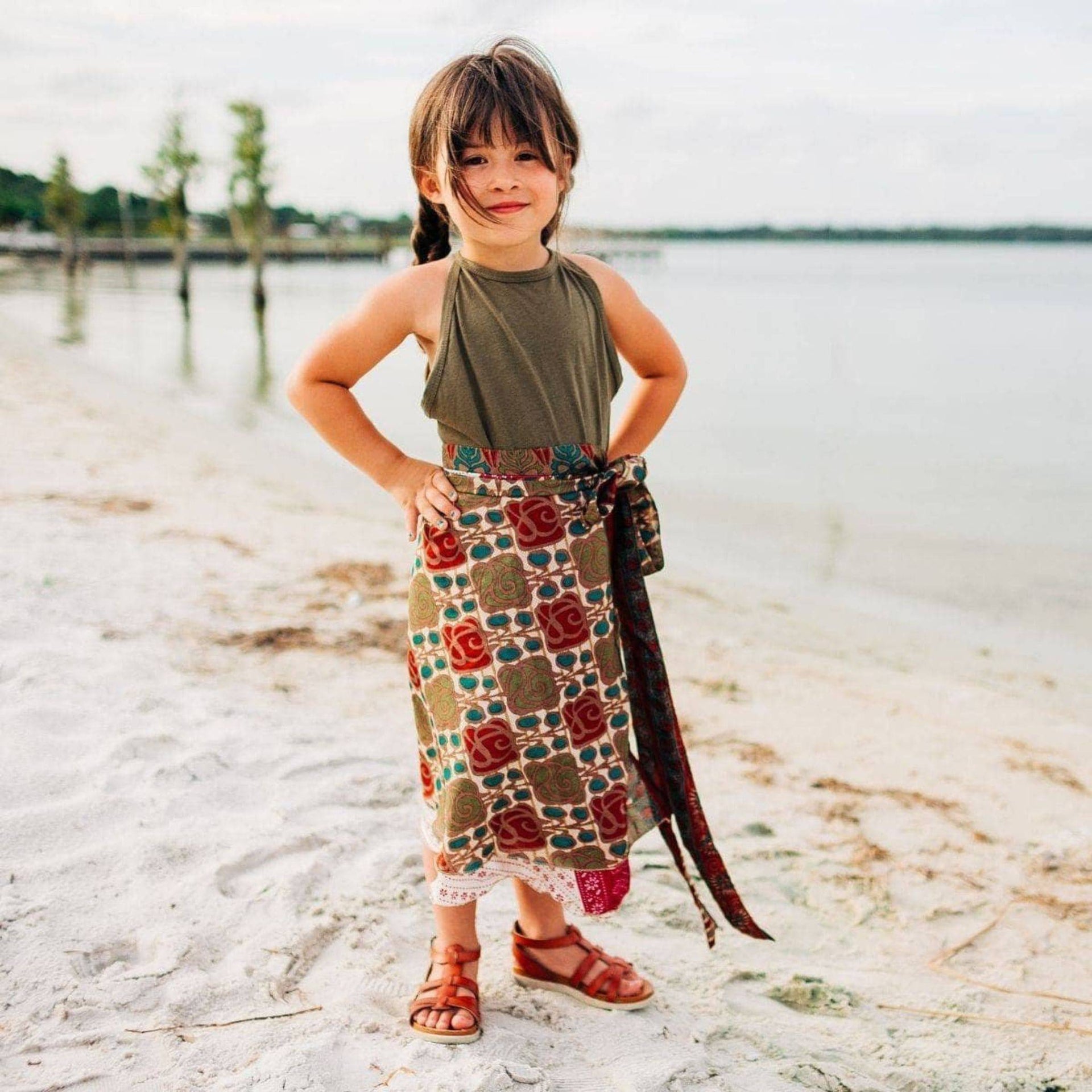 A child wearing a vibrant, bohemian, knee-length reversible silk skirt with a tie closure in a natural setting.