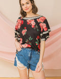 A woman wearing a black floral print bohemian top with tiered ruffle sleeves and red rose patterns.