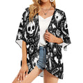 A woman wearing a lightweight black and white chiffon kimono with an all-over skull and gothic pattern, styled open over a white camisole.