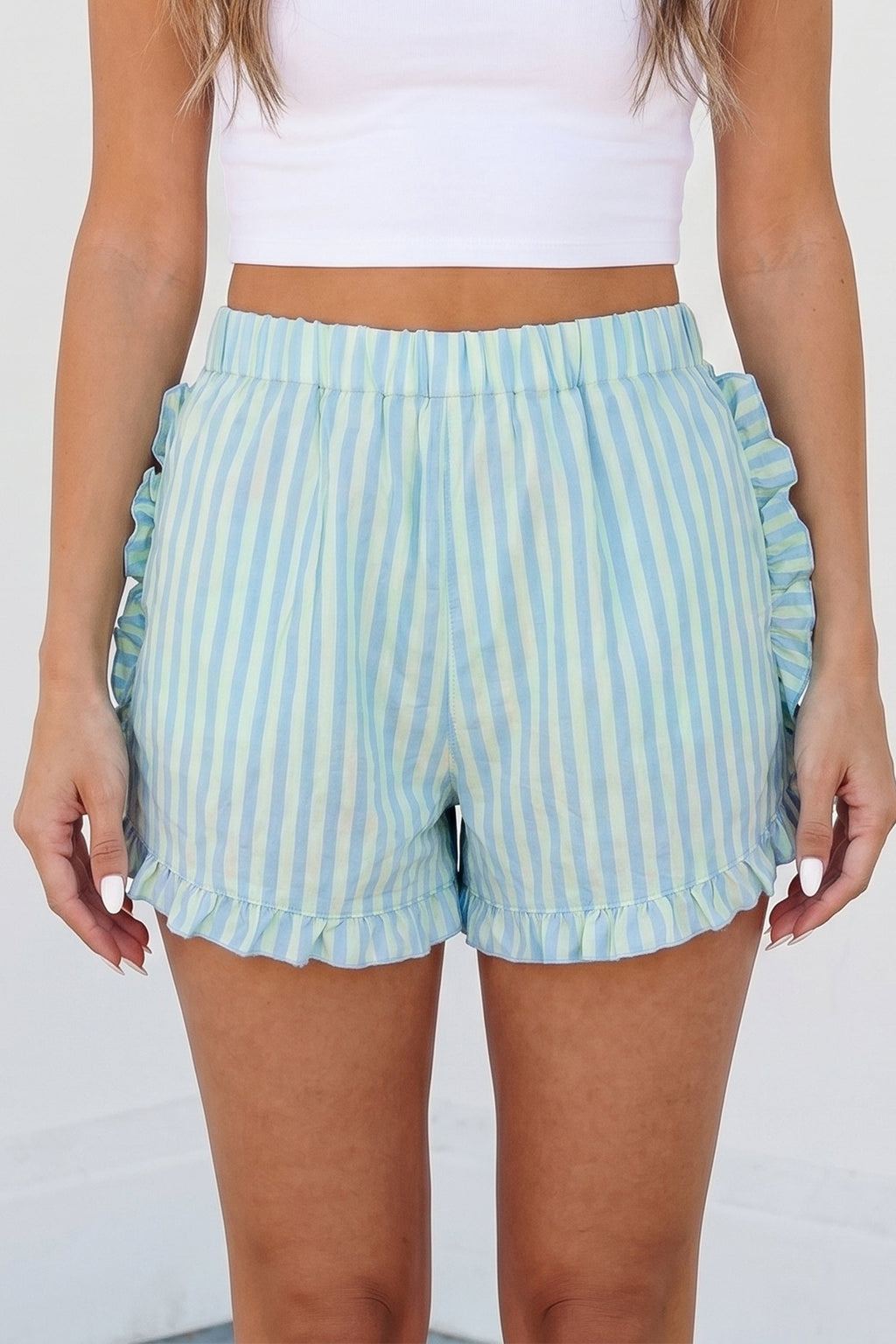 A pair of light blue and pale yellow vertical striped cotton shorts with a ruffled hem and elastic waistband.