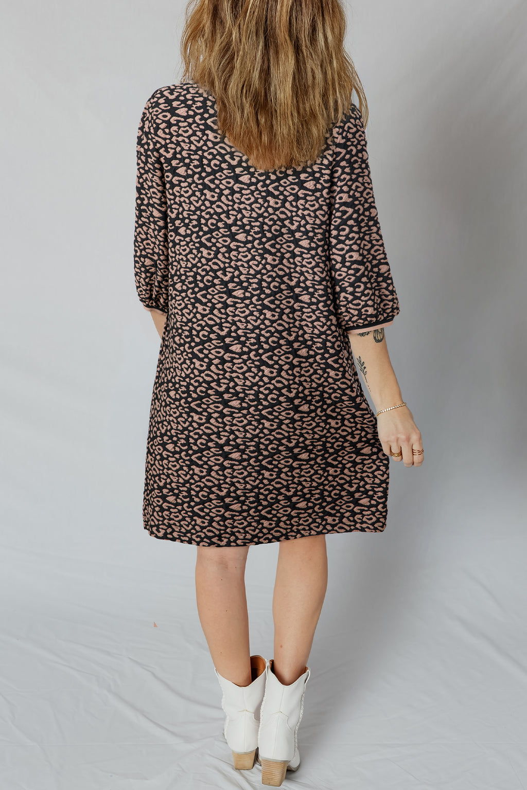 Person wearing a leopard print dress with white boots on a plain background