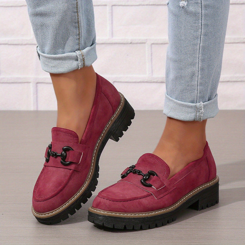 A pair of burgundy horsebit loafers with a chunky black lug sole worn with light blue cuffed jeans.