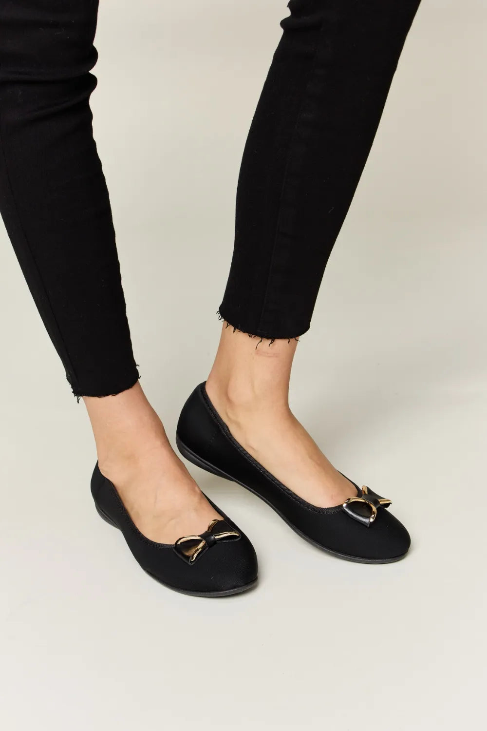 A pair of black women's flat loafers with a gold metal buckle detail viewed from the side