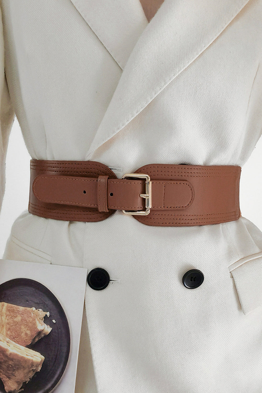 Close up of a brown wide elastic PU belt with a gold-tone zinc alloy buckle worn over a white blazer.