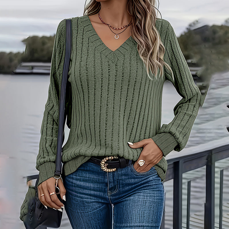A woman wearing a long-sleeved olive green ribbed knit V-neck blouse styled with jeans