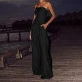 Model wearing a minimalist black strapless wide-leg jumpsuit in a relaxed resort-style setting