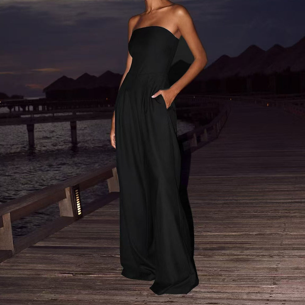Model wearing a minimalist black strapless wide-leg jumpsuit in a relaxed resort-style setting