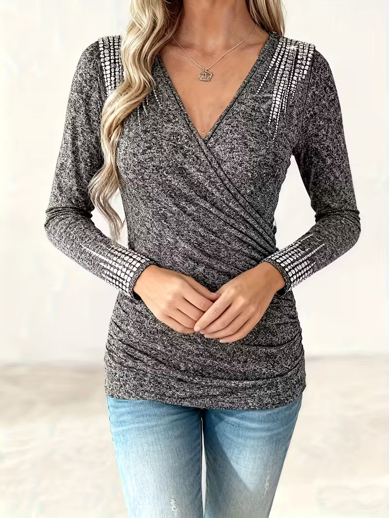A woman wearing a grey long-sleeve V-neck wrap top with rhinestone embellishments on the shoulders and cuffs.