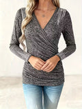 A woman wearing a grey long-sleeve V-neck wrap top with rhinestone embellishments on the shoulders and cuffs.