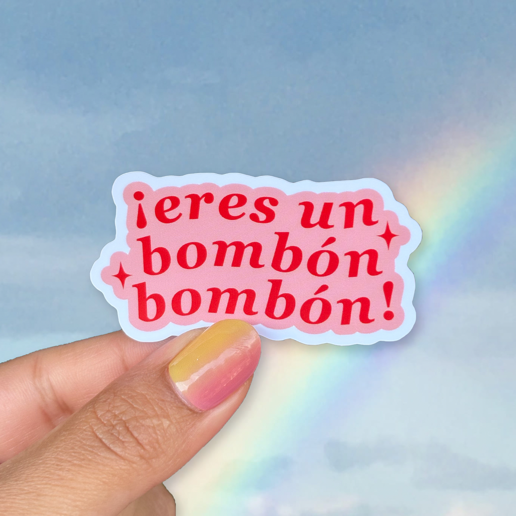 Sticker with Spanish text held by a hand against a rainbow-lit background
