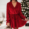 A woman wearing a long sleeve velvet v-neck mini dress with a tied waist, shown in red and dark green.