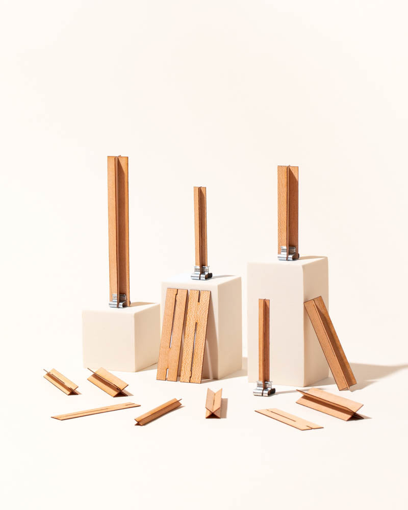 Collection of X-shaped wooden candle wicks with metal base clips standing on white pedestals