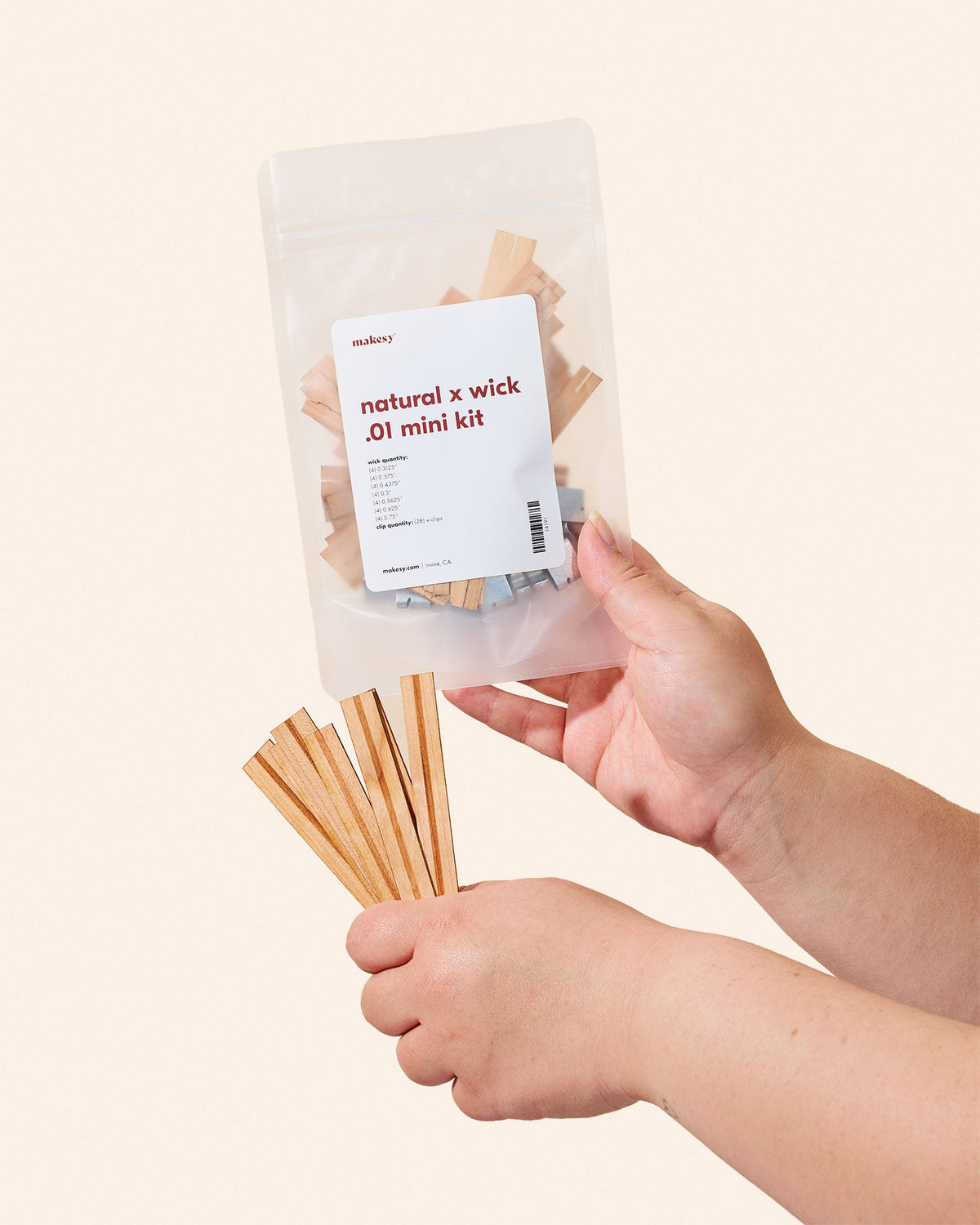 A person holding a transparent bag filled with various sizes of natural wood wicks and metal clips for candle making.