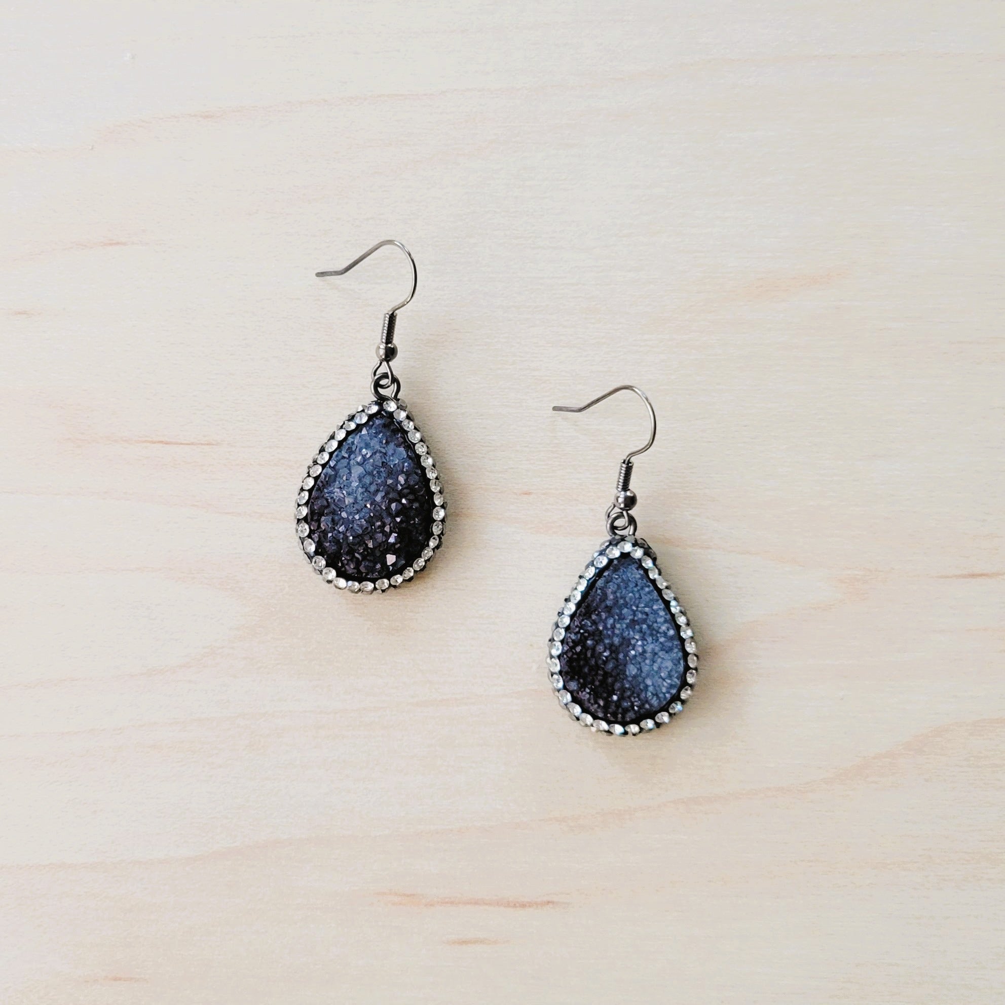 A pair of black teardrop druzy earrings surrounded by small crystals on silver-tone fishhook wires.