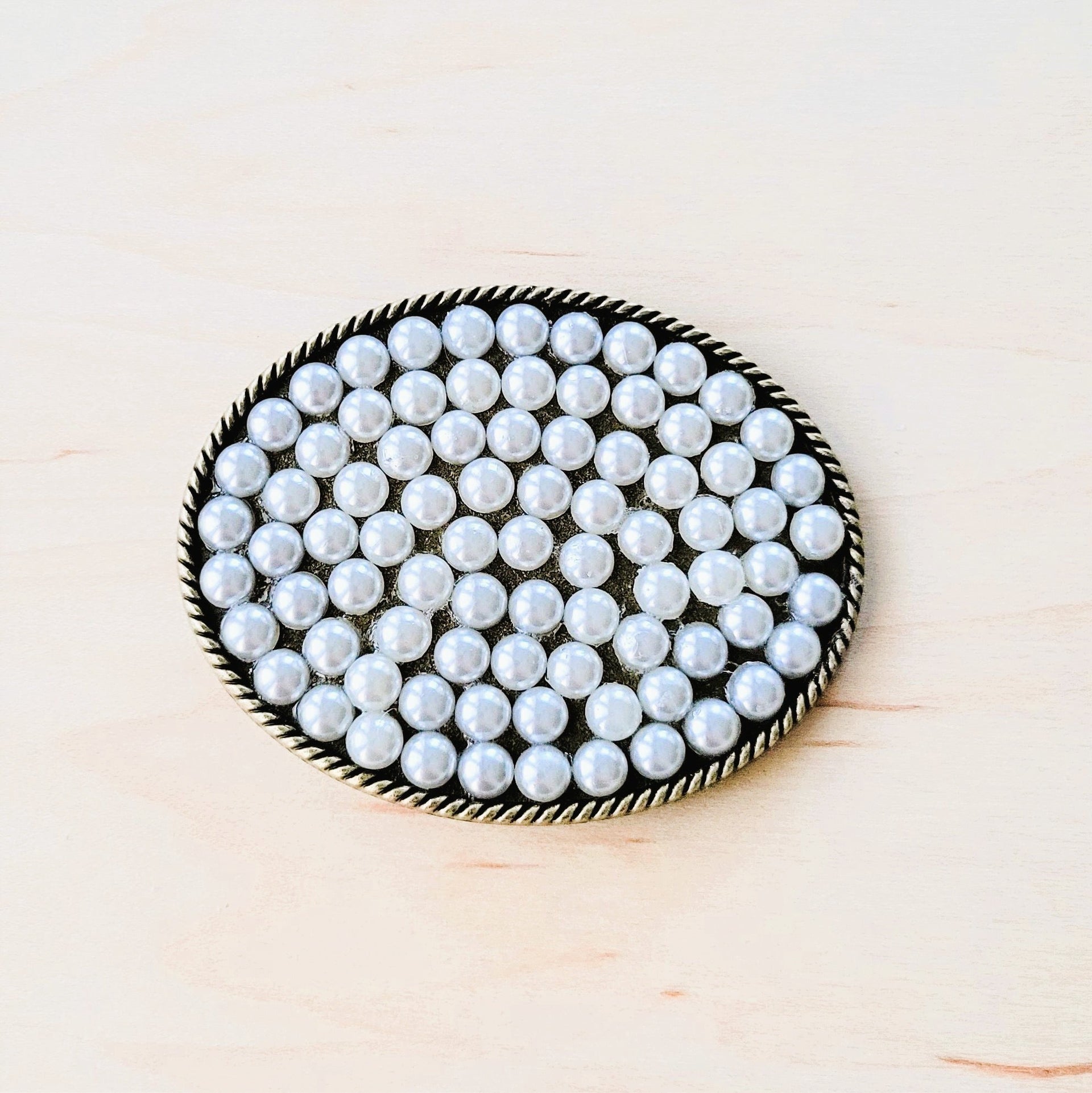 Oval shaped antique gold-tone belt buckle with a rope border and white pearl bead inlay