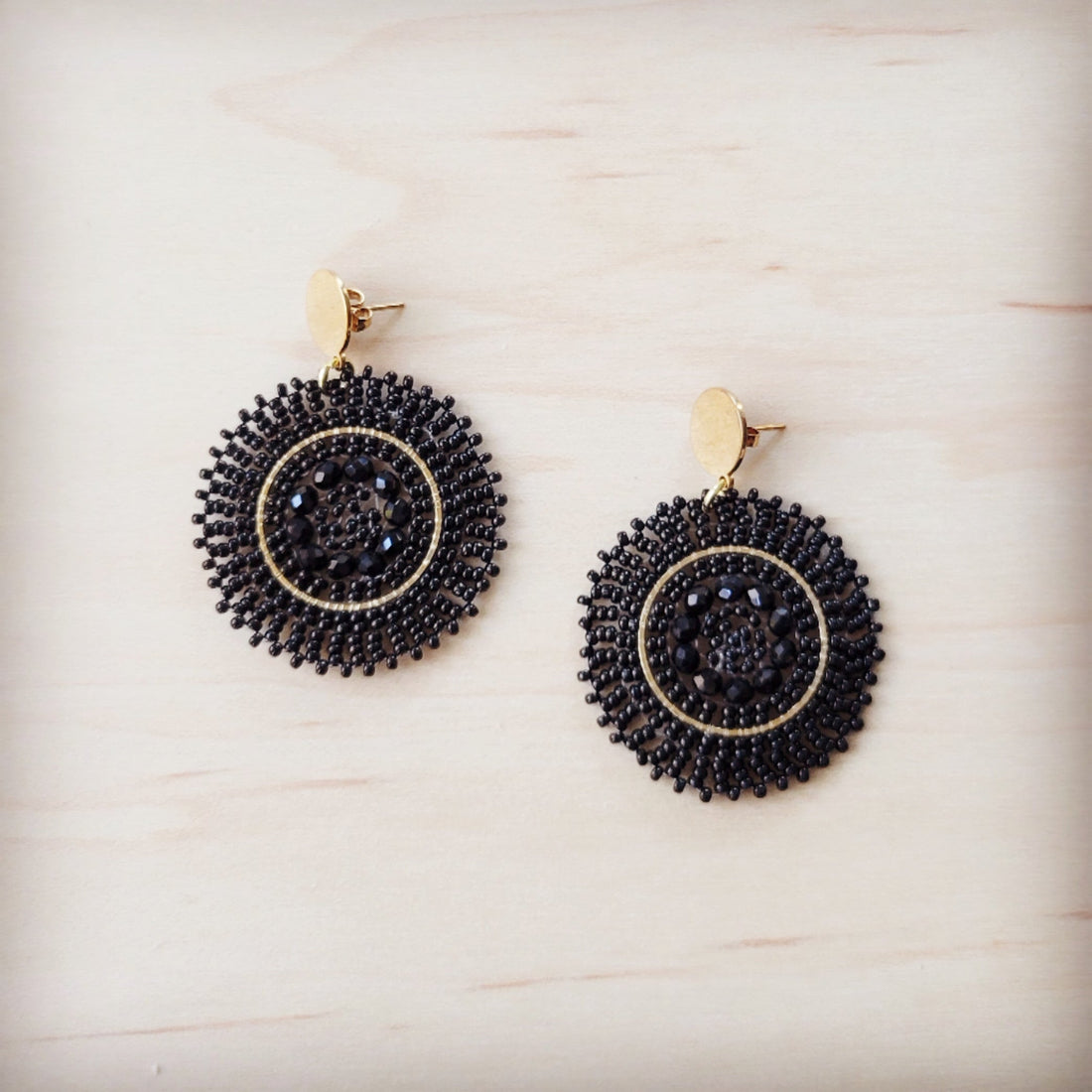 A pair of gold-tone post dangle earrings with a circular medallion drop featuring woven ebony beads and black center crystals.