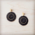 A pair of gold-tone post dangle earrings with a circular medallion drop featuring woven ebony beads and black center crystals.