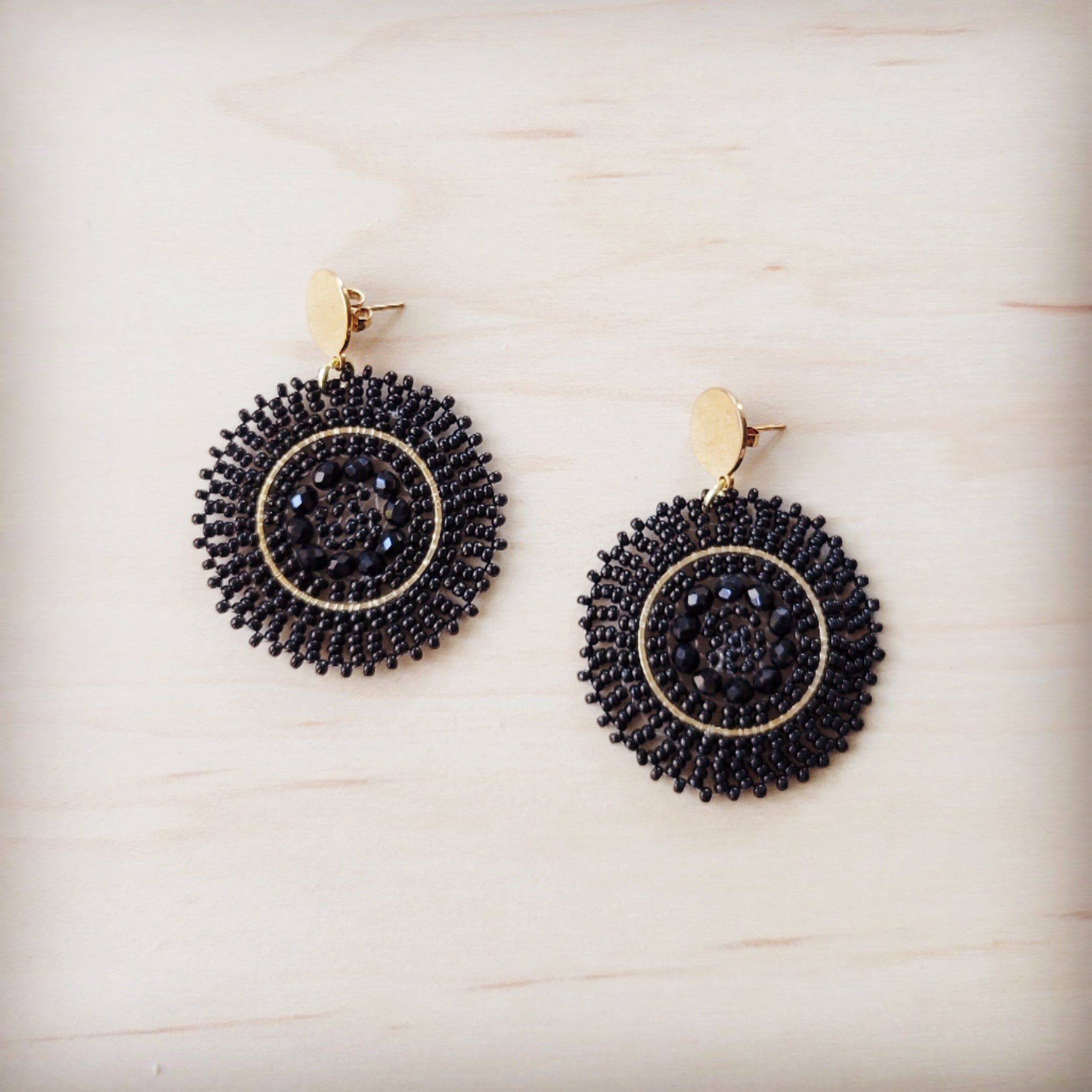 A pair of gold-tone post dangle earrings with a circular medallion drop featuring woven ebony beads and black center crystals.