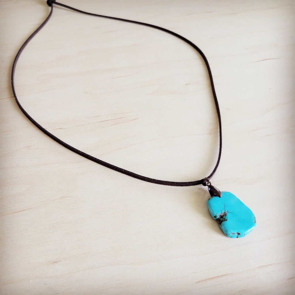 Genuine turquoise slab pendant hanging on a brown leather cord necklace on a wood surface