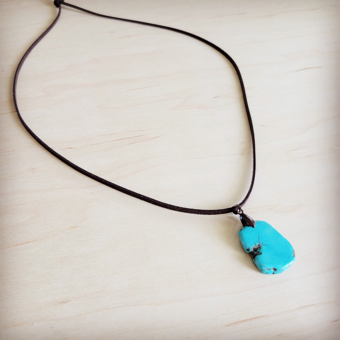 Genuine turquoise slab pendant hanging on a brown leather cord necklace on a wood surface