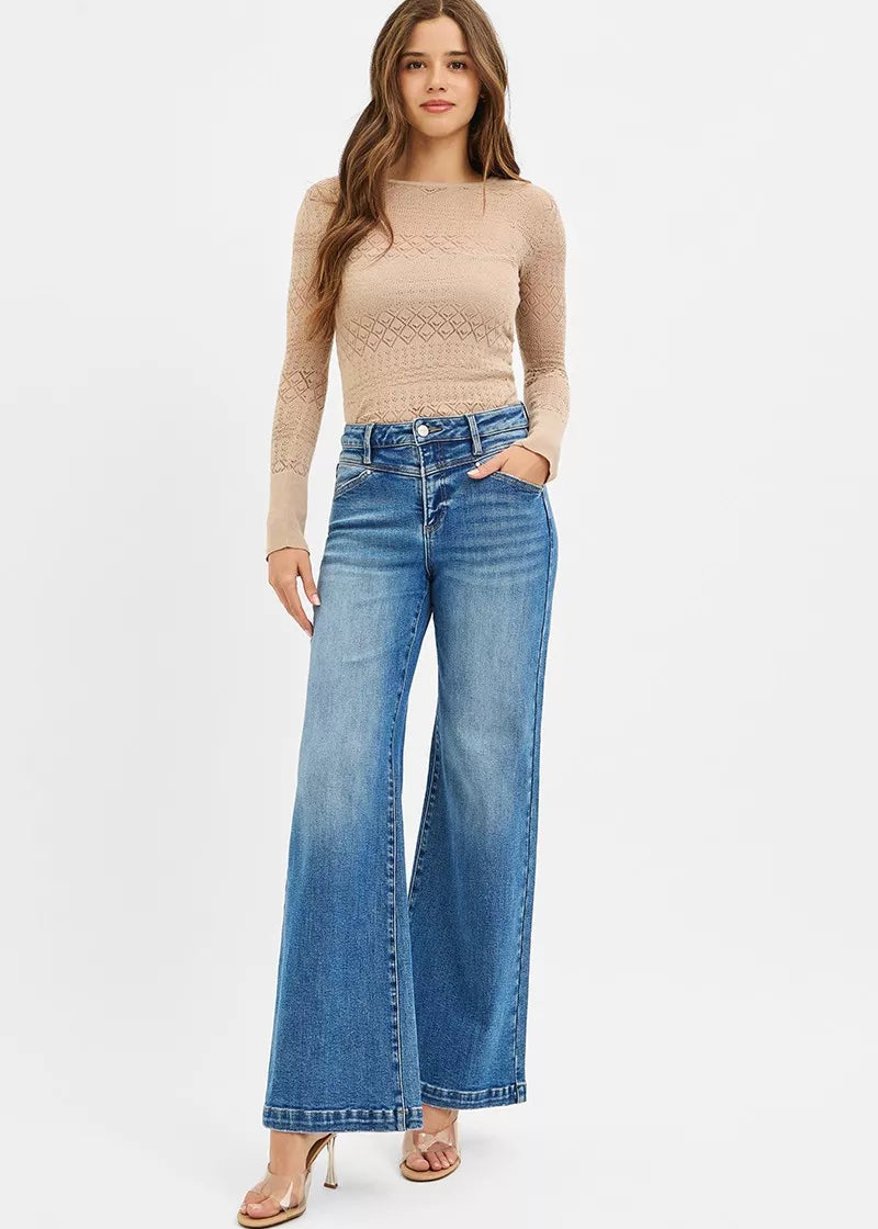 Woman wearing a beige long-sleeve top and blue jeans on a white background