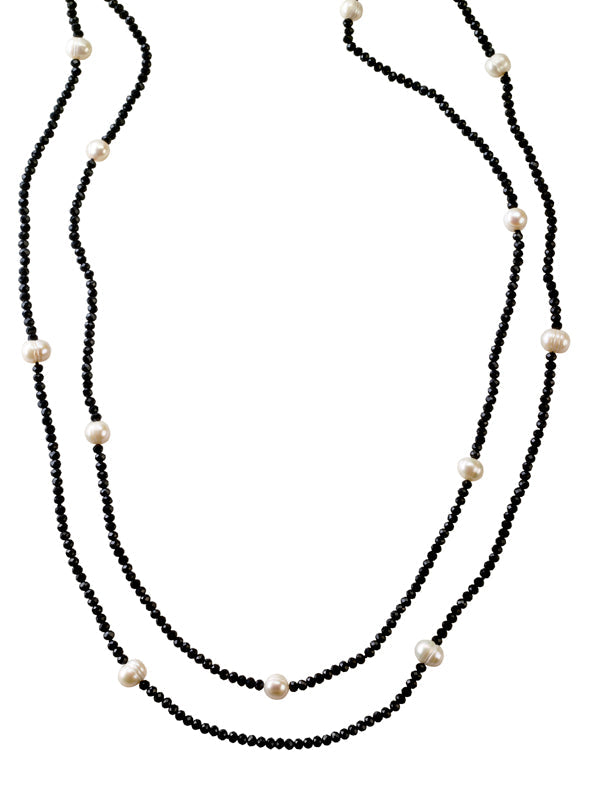 Model wearing a long black crystal and freshwater pearl necklace set layered over a taupe dress