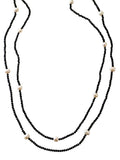 Model wearing a long black crystal and freshwater pearl necklace set layered over a taupe dress