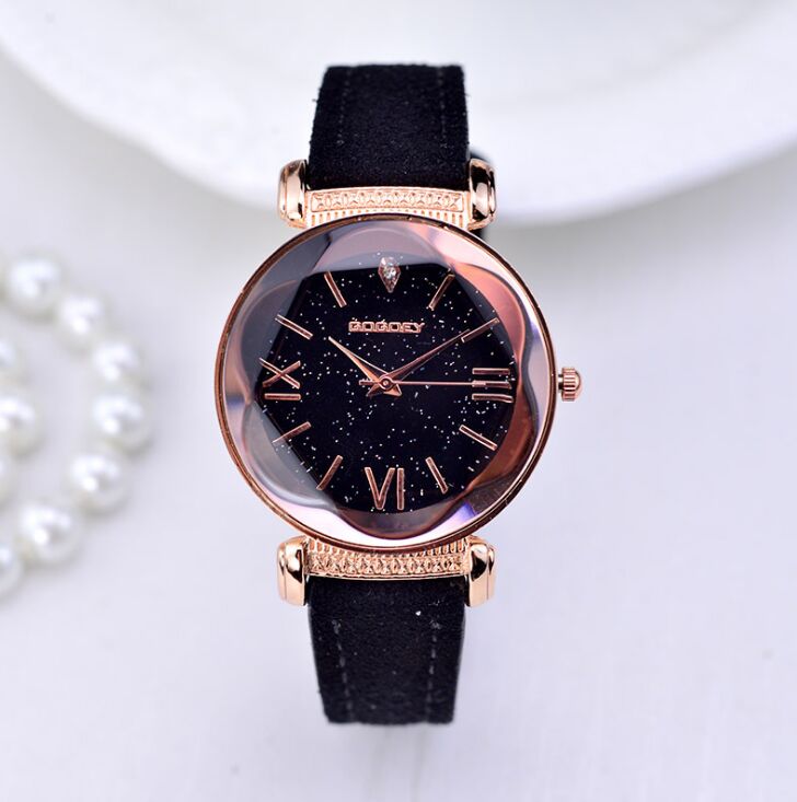 Close-up of a women's rose gold watch with a black starry dial and black leather strap, alongside pearls