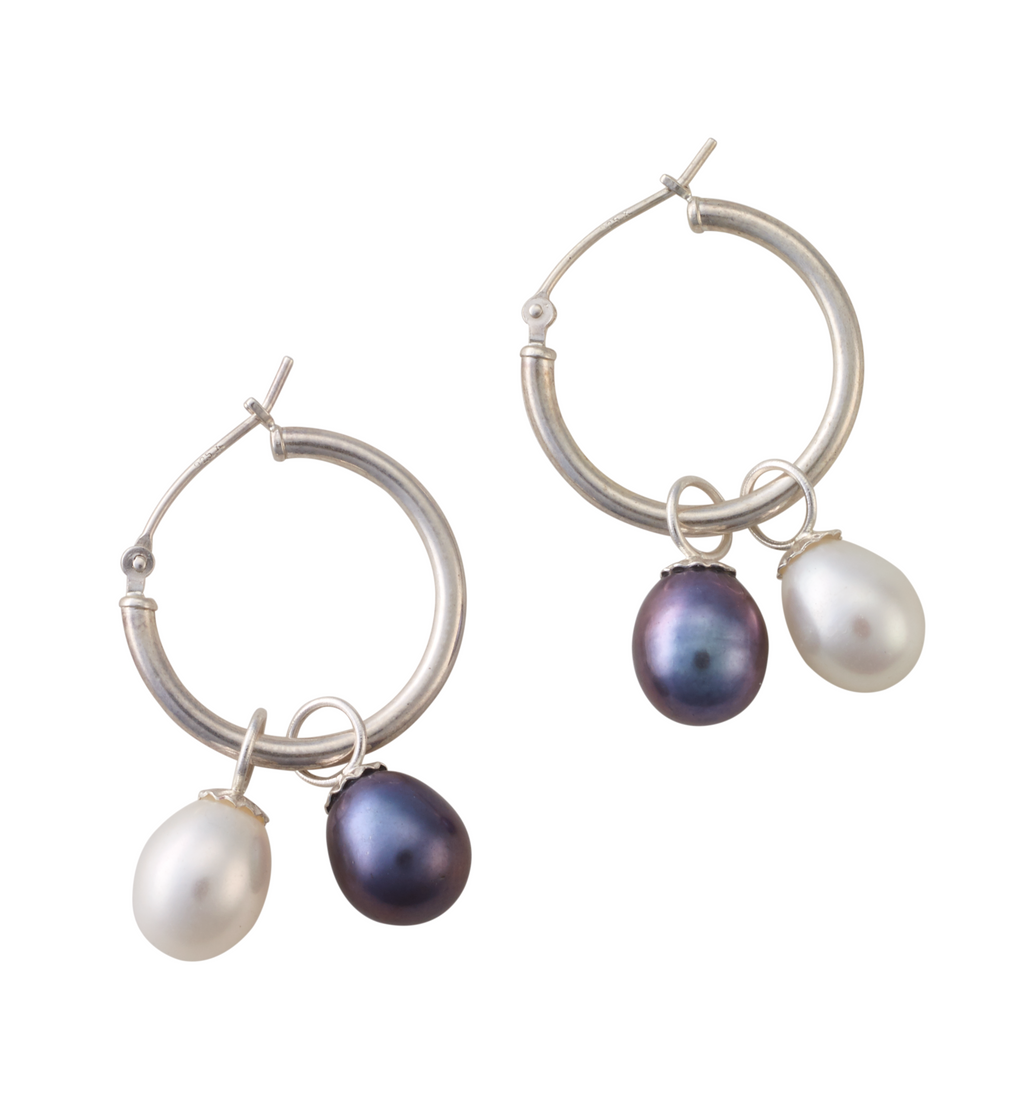 A pair of silver hoop earrings each holding one white freshwater pearl and one black freshwater pearl.