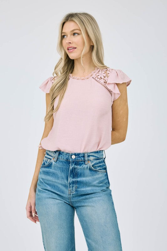 Woman wearing a lightweight woven blouse featuring ruffle sleeves and delicate lace shoulder panels.