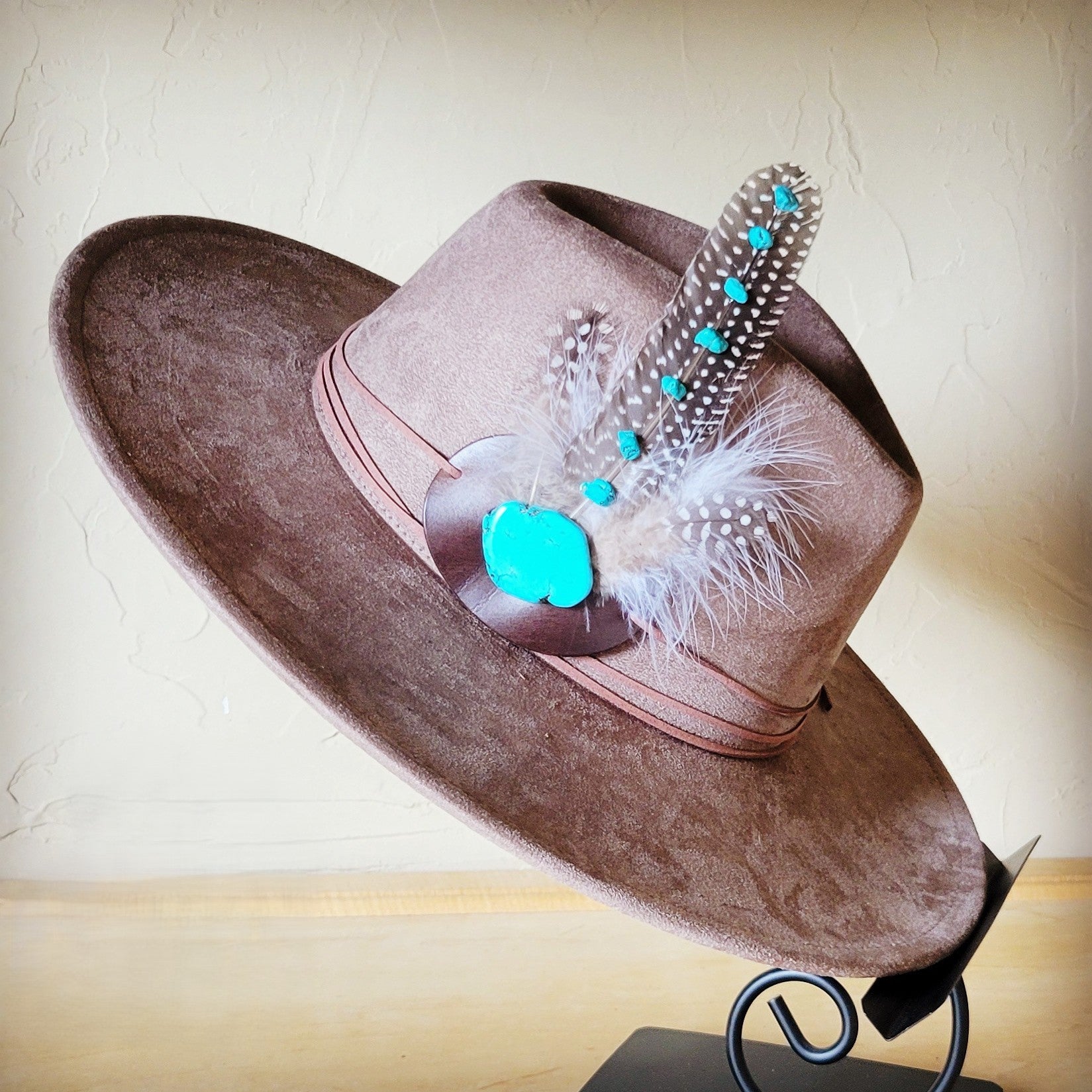 A taupe colored felt western style hat decorated with a decorative hat band featuring natural feathers and turquoise stone accents.