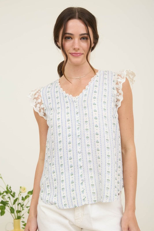 Woman wearing a striped floral V-neck blouse with lace trim and ruffle sleeves in white, blue, and green.