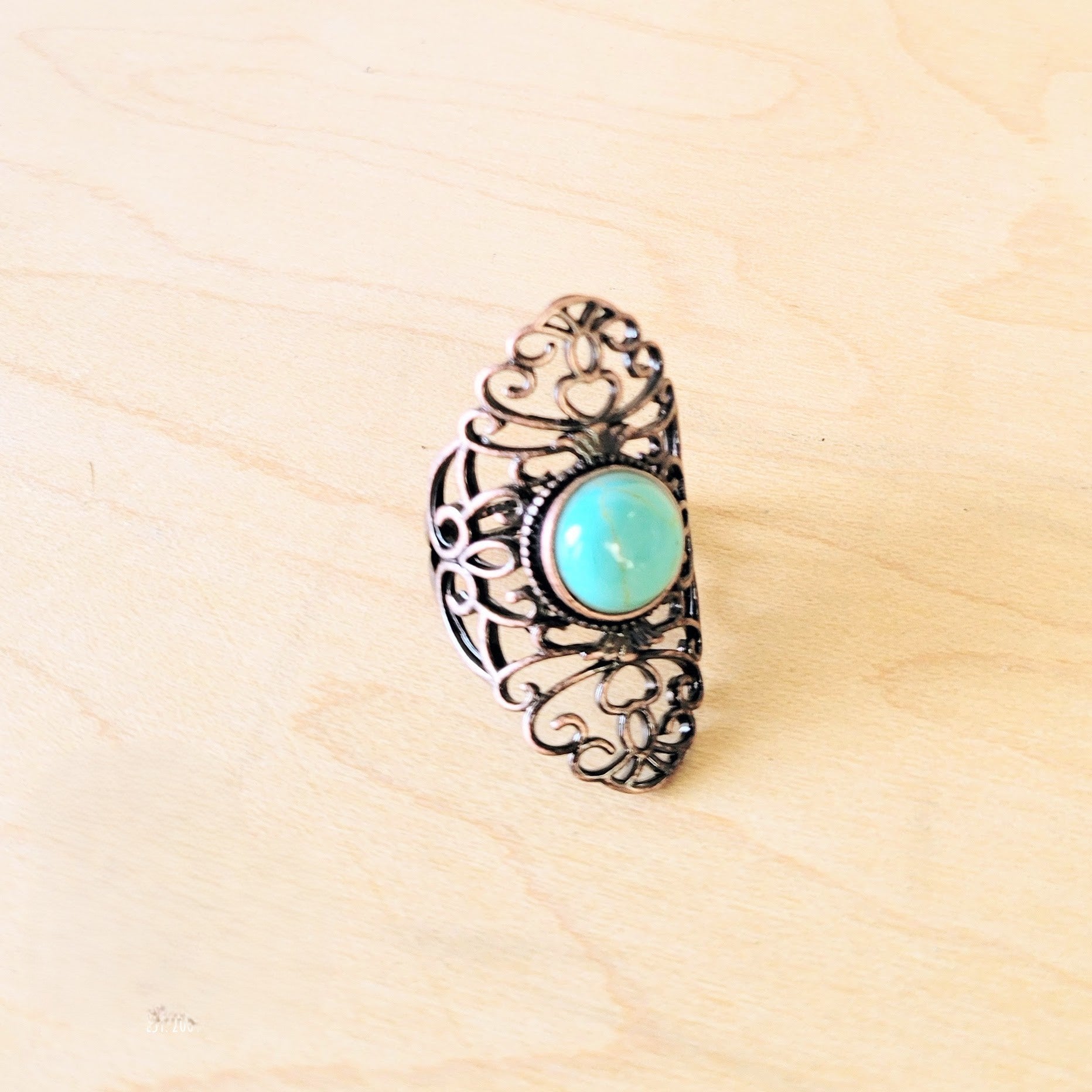Blue turquoise ring in an antique copper filigree setting on a light wooden background