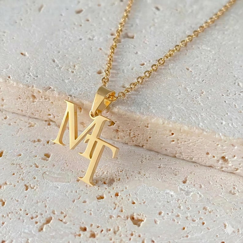 Close-up of a custom gold-tone interwoven letter necklace featuring elegant script initials.