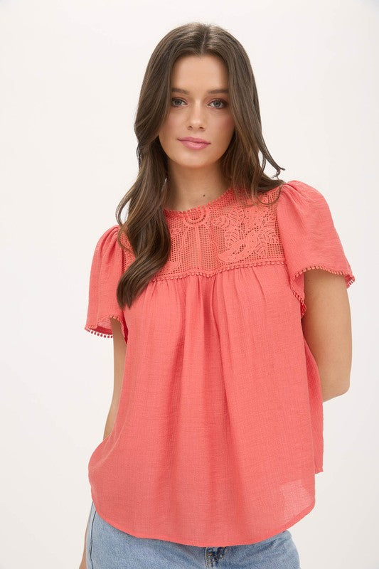Close up of a blouse with sheer lace yoke, ruffle sleeves, and pom pom trim details.