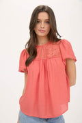 Close up of a blouse with sheer lace yoke, ruffle sleeves, and pom pom trim details.