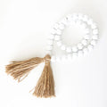White wooden bead garland with brown jute tassels on a white background