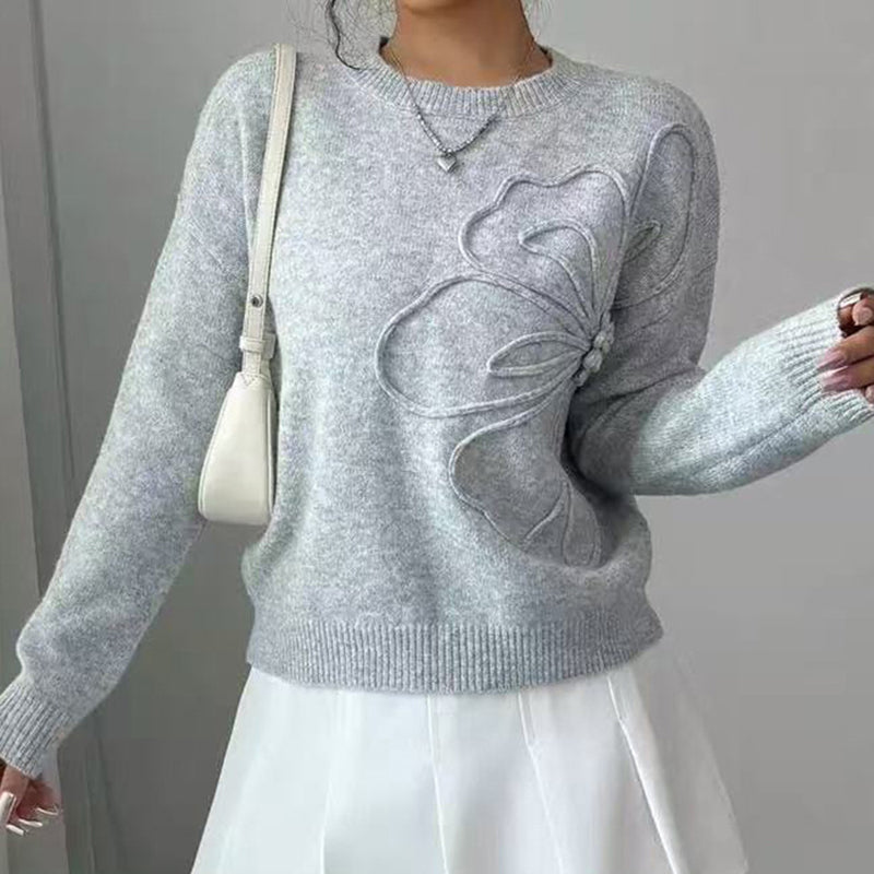 Women's elegant grey knit sweater featuring a prominent raised floral applique on the chest, worn with a white skirt.