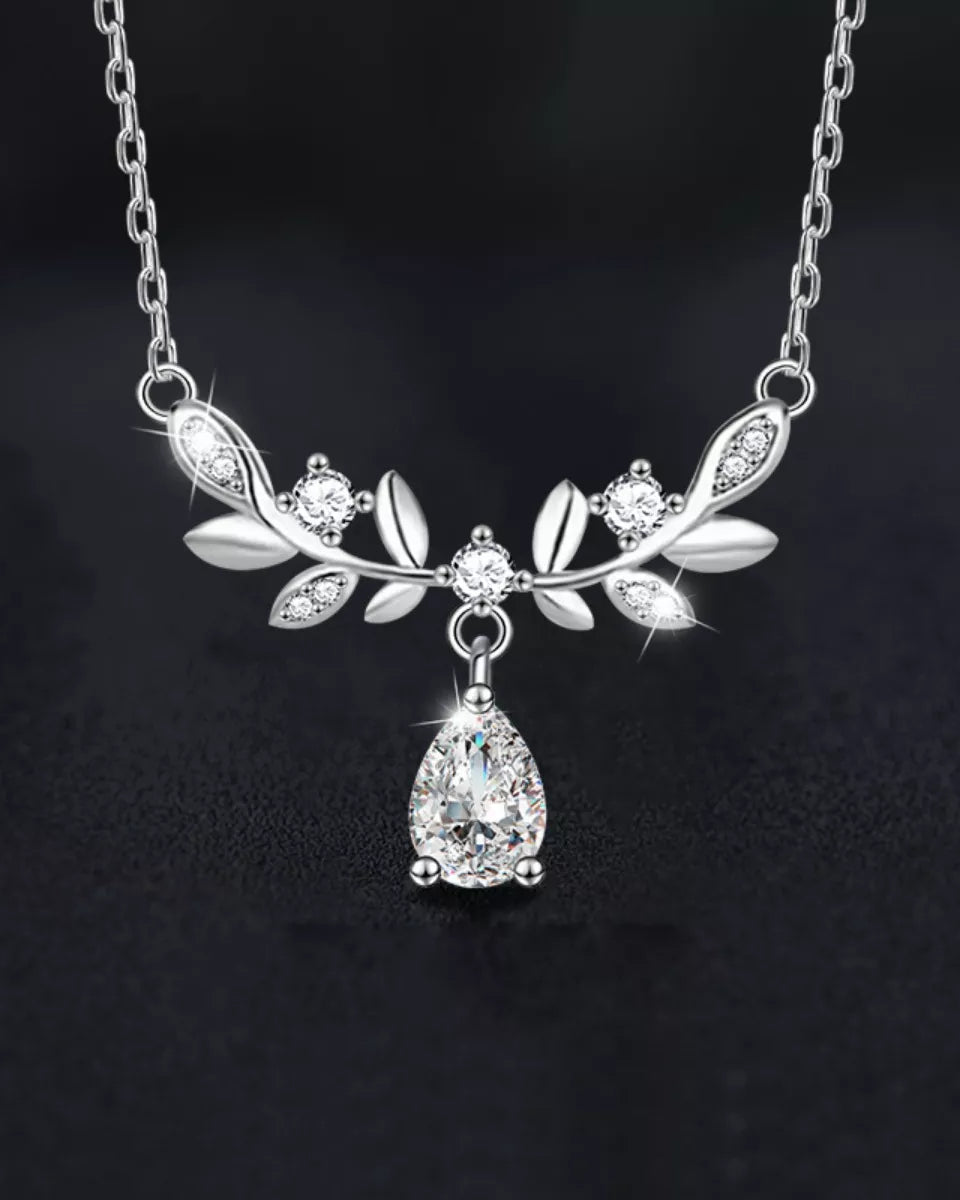 Silver necklace with leaf design and teardrop pendant on a dark background