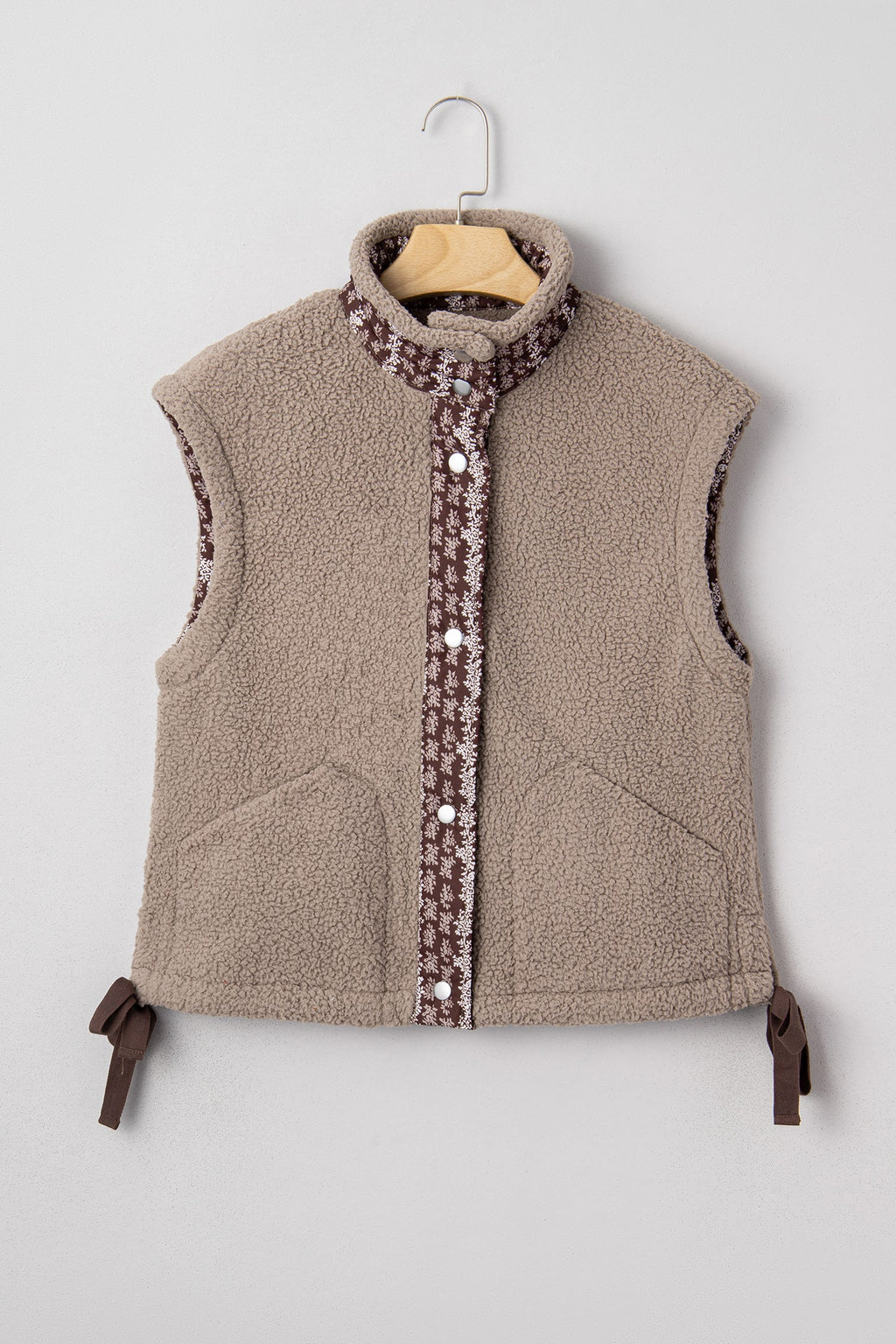 Tan sherpa fleece vest with brown and white floral trim, front button closure, and side ribbon bows.