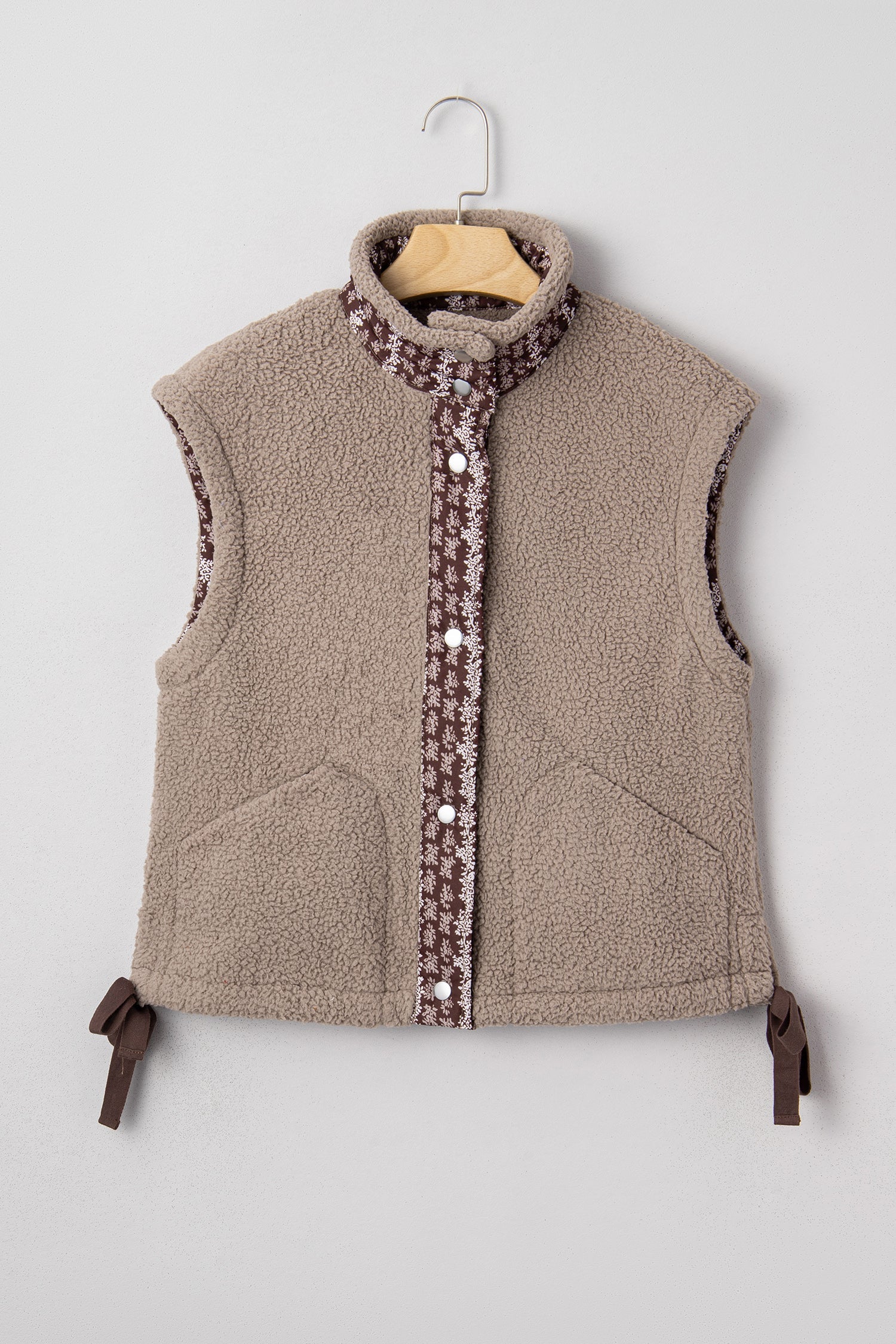 Tan sherpa fleece vest with brown and white floral trim, front button closure, and side ribbon bows.